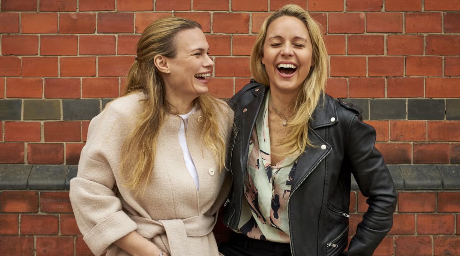 Angelika och Ida skrattar framför en tegelvägg